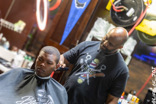 A Blade Barbershop barber lines up a young client under the neon ring light during the 888 Fresh Start Experience.
