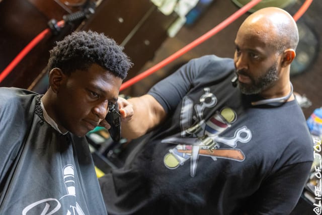 A barber shapes a client's hair under the red neon of the lounge during the 888 Fresh Start Experience.